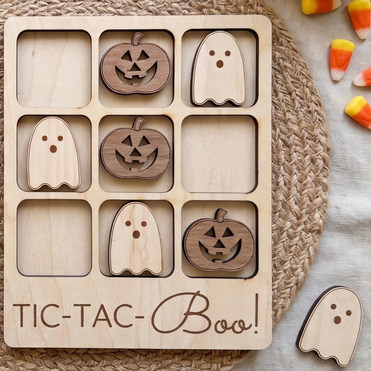 A wooden tic-tac-toe game board with carved pumpkin and ghost pieces, along with a spooky Halloween-themed game board and candy.