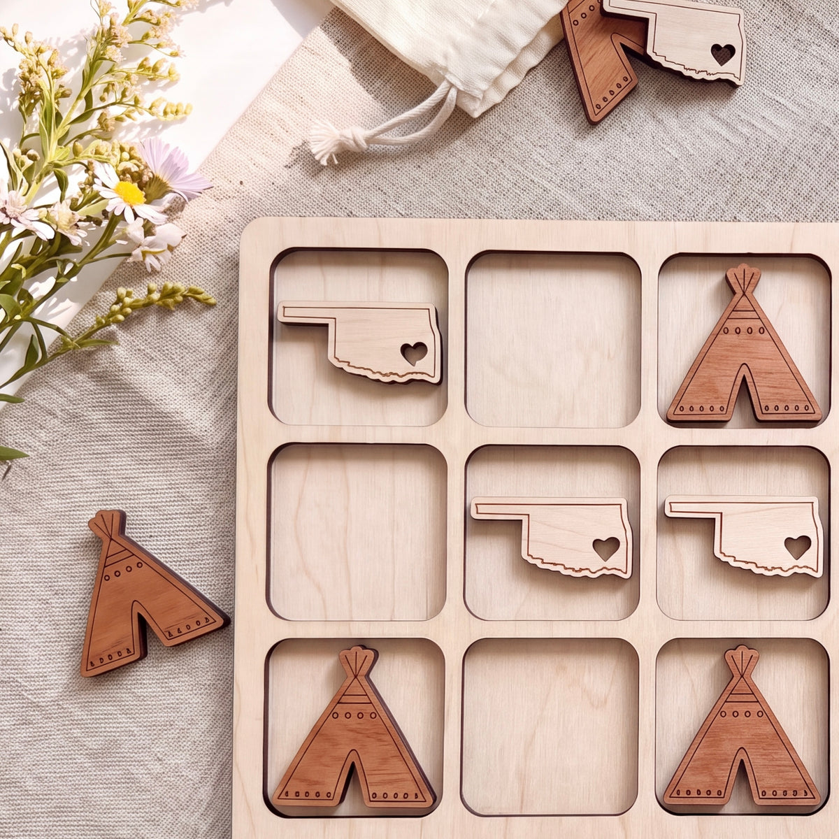 a wooden tic-tac-toe board with wooden cut-out shapes representing the states of Oklahoma and Texas. There are also wooden cut-out shapes resembling teepees, which are placed on the board.