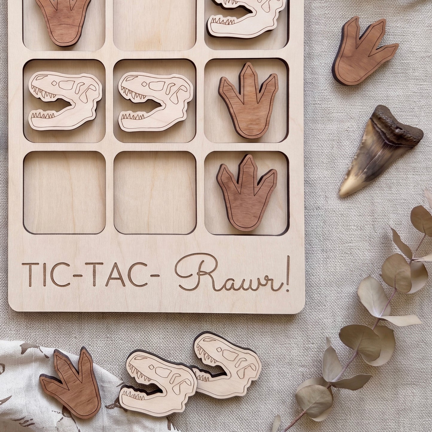 a wooden game board with dinosaur claw and tooth-shaped tiles, along with a few dinosaur claw and tooth-shaped tiles scattered around it.
