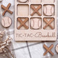 A wooden tic-tac game board labeled "TIC-TAC-Baseball" with wooden bats and baseballs on it, along with some additional wooden bats and baseballs scattered around.
