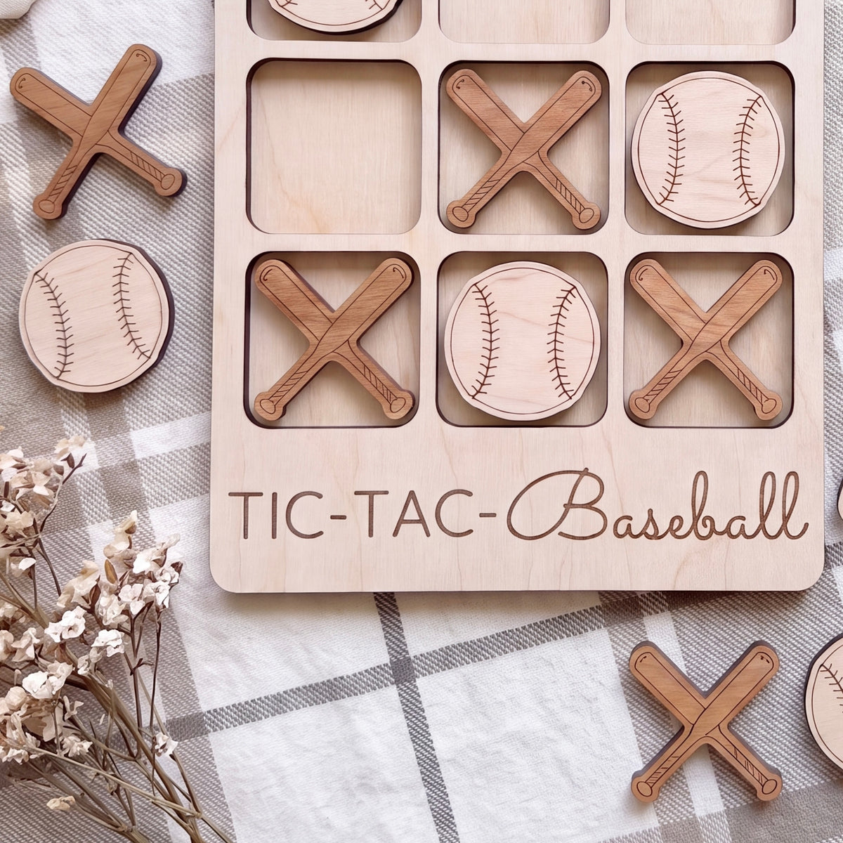 A wooden tic-tac game board labeled "TIC-TAC-Baseball" with wooden bats and baseballs on it, along with some additional wooden bats and baseballs scattered around.