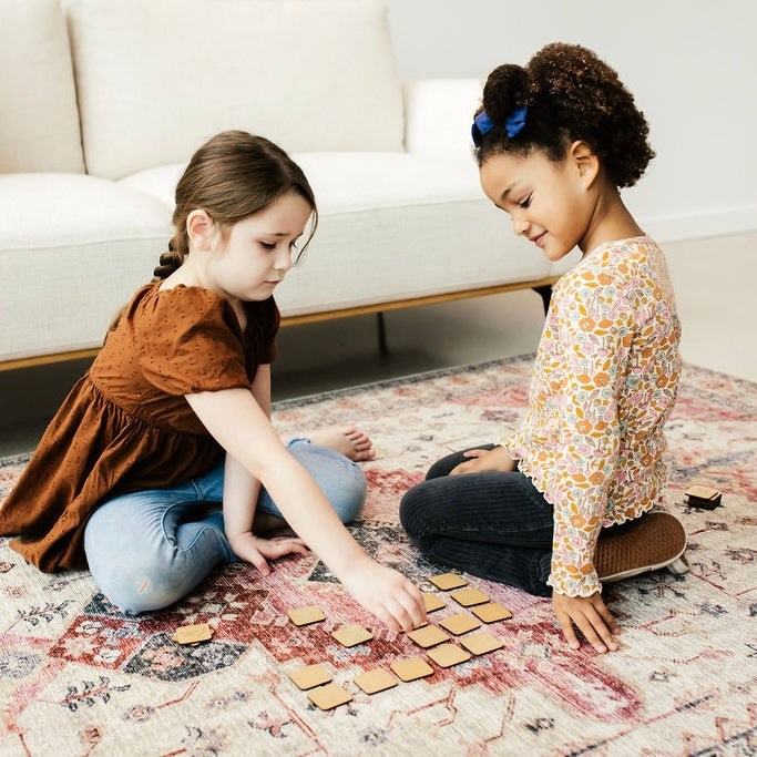 Two young girls are sitting on the floor, playing with wooden blocks.