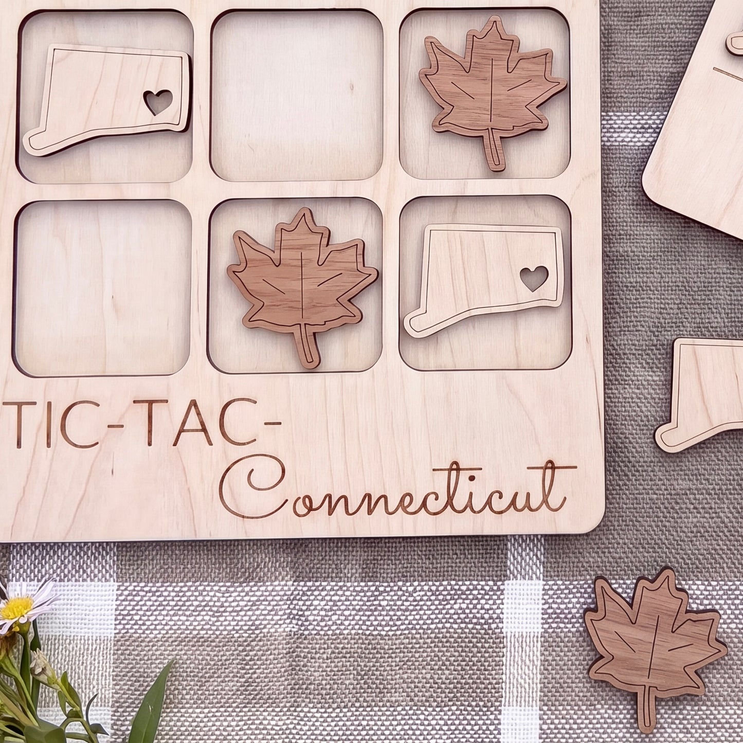 a wooden tic-tac game board with wooden pieces shaped like leaves and states, specifically Connecticut, placed on it.