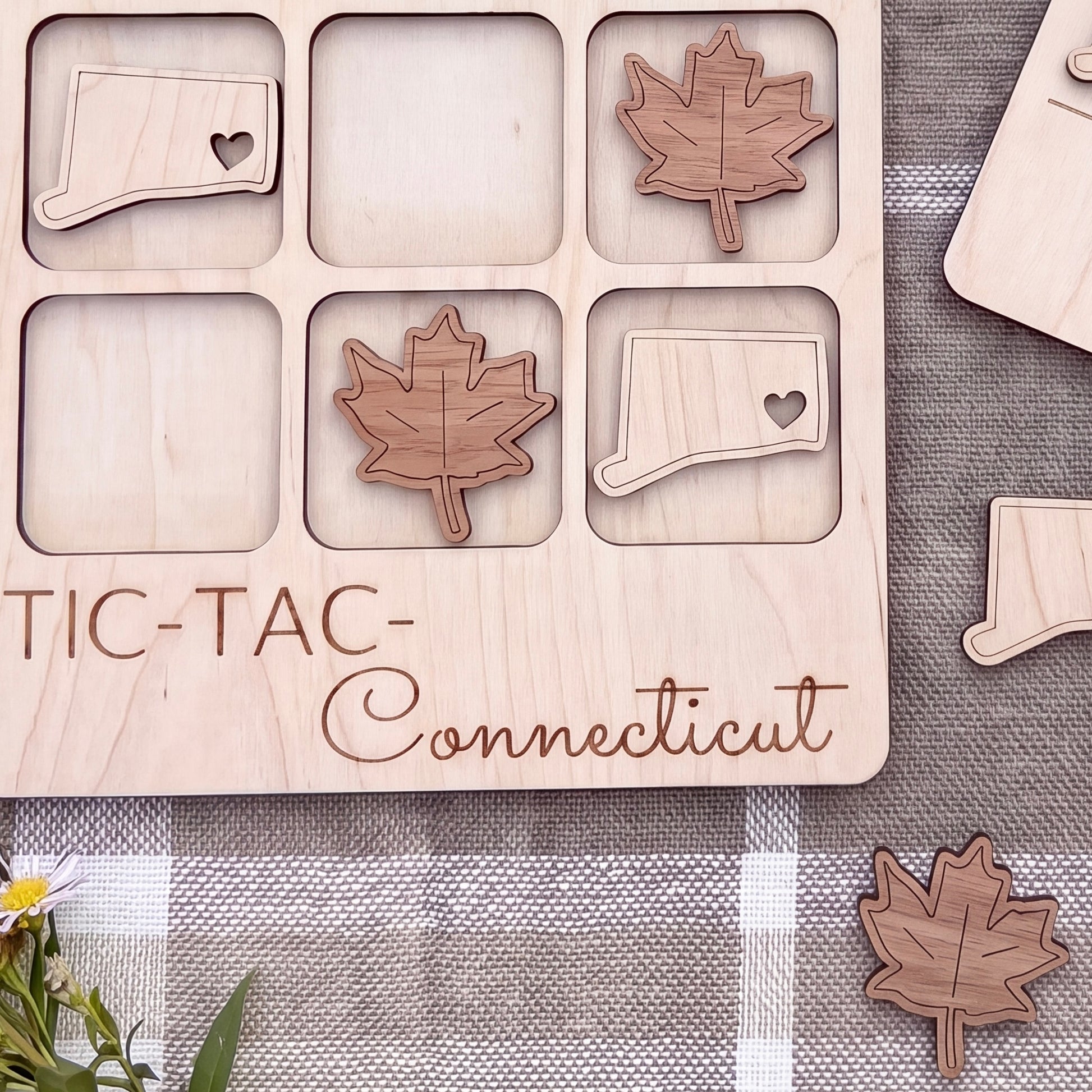 a wooden tic-tac game board with wooden pieces shaped like leaves and states, specifically Connecticut, placed on it.