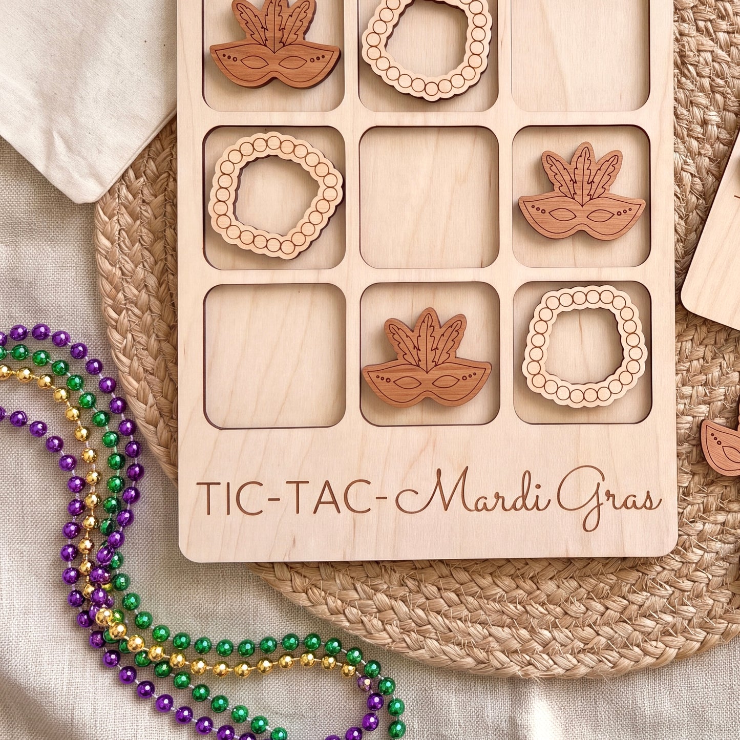 a wooden tic-tac game with wooden pieces shaped like beads and masks, placed on a woven placemat. There are also beads of different colors, including purple, green, and gold, scattered around the game.