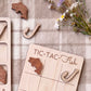 a wooden game board with a fish-shaped tile and a hook-shaped tile, along with some flowers and a plaid cloth.