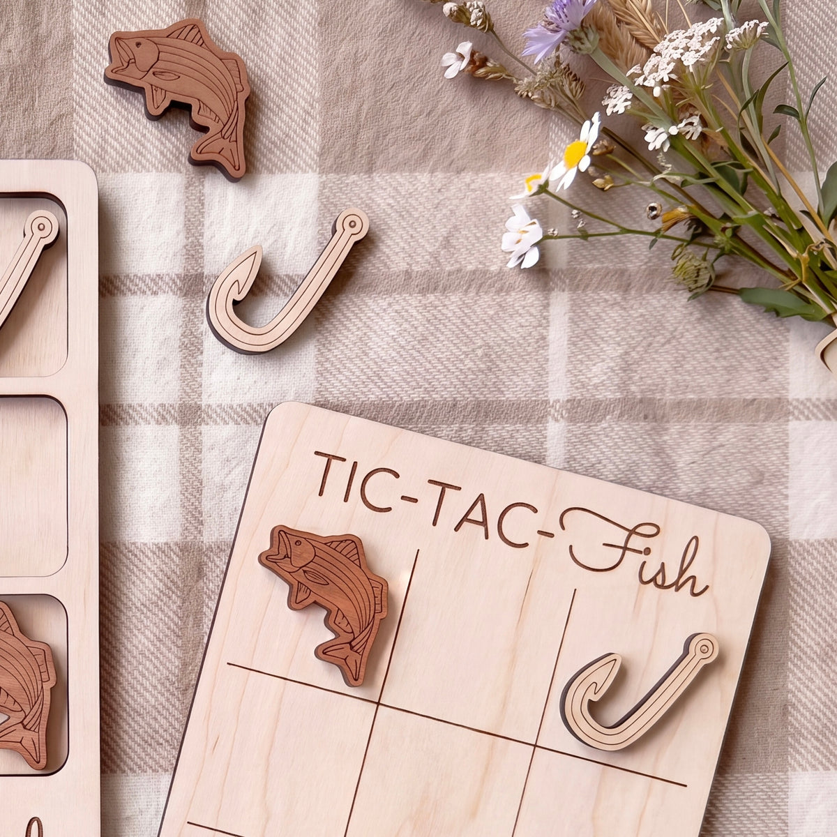a wooden game board with a fish-shaped tile and a hook-shaped tile, along with some flowers and a plaid cloth.