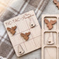 A wooden tic-tac game board with wooden moose and heart-shaped pieces, placed on a blanket with a plaid pattern.