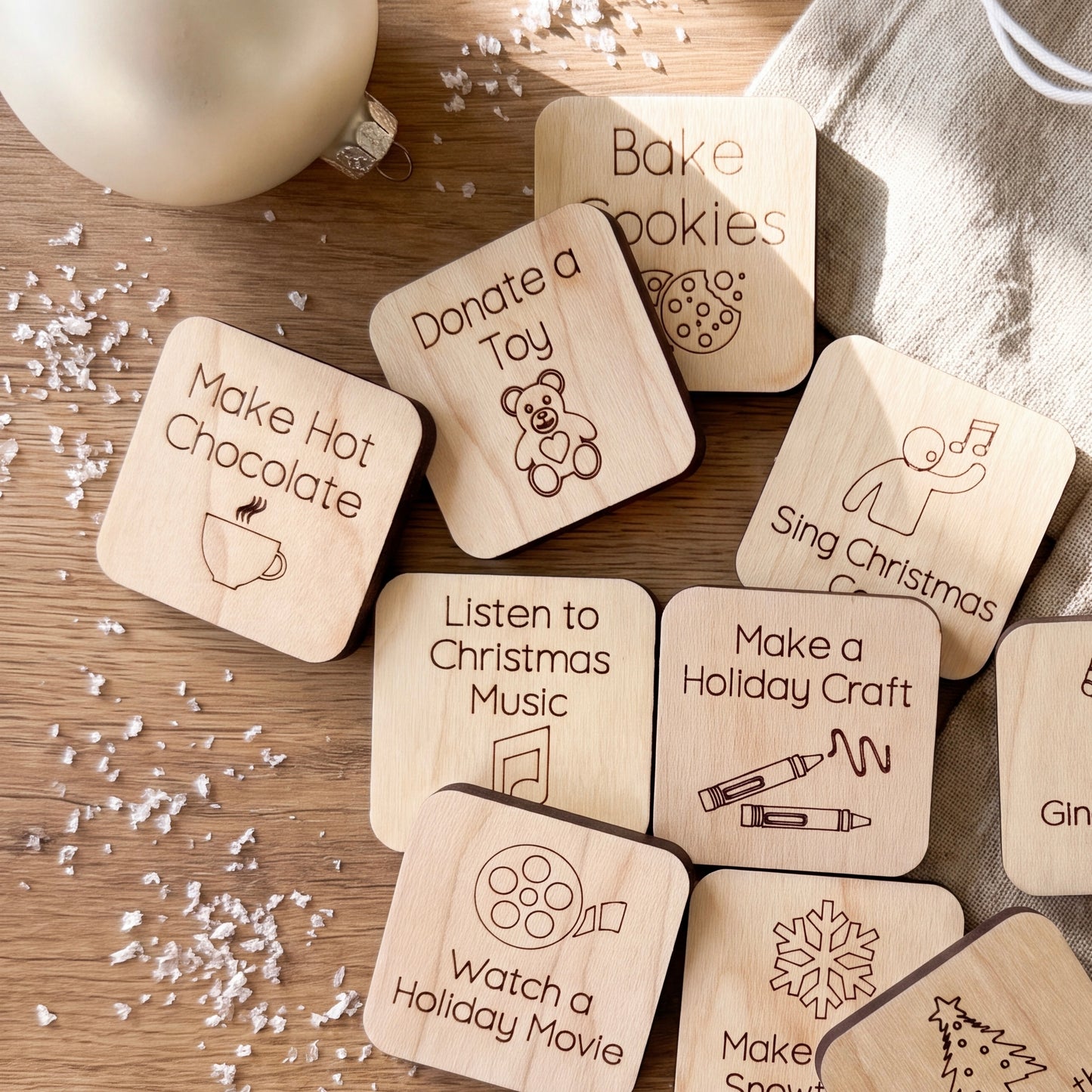 a collection of wooden coasters with various holiday-themed activities and items written on them, placed on a wooden surface with scattered white snowflakes.