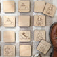 a collection of wooden coaster-shaped objects with various symbols and designs, including a lantern, a fire, a mountain, and a hiking boot.