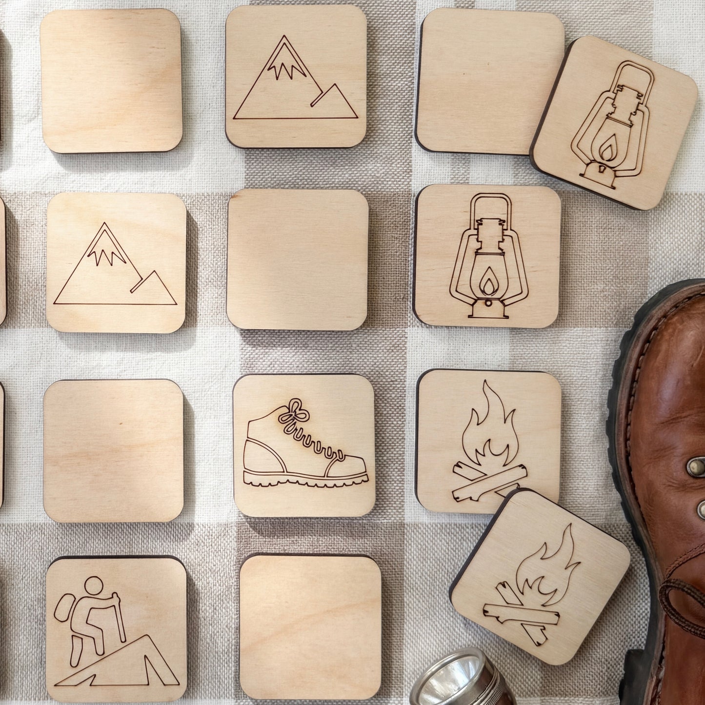 a collection of wooden coaster-shaped objects with various symbols and designs, including a lantern, a fire, a mountain, and a hiking boot.