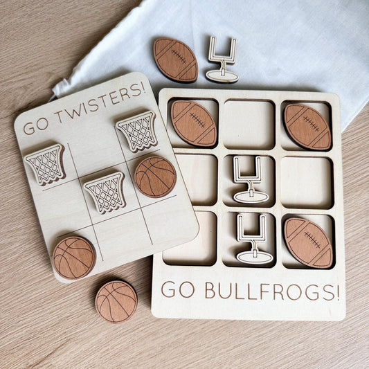 a wooden game board with various sports-themed tiles, including a basketball, football, and a teddy bear, along with a teddy bear and a football. The game board also has a sign that says "Go Bullfrogs!"