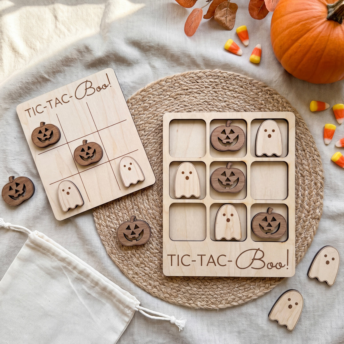 a wooden tic-tac game with carved pumpkin and ghost pieces, along with a pumpkin and candy corn on a woven placemat.