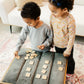 Two young children, a boy and a girl, are playing with wooden blocks on a gray couch.