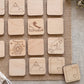 a collection of wooden coasters or tiles with various symbols and designs, including a mountain, a shoe, a cat, and other abstract shapes.
