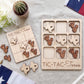 a wooden Tic-Tac-Texas game board and several wooden tiles shaped like the state of Texas, along with a potted cactus plant and a flag.