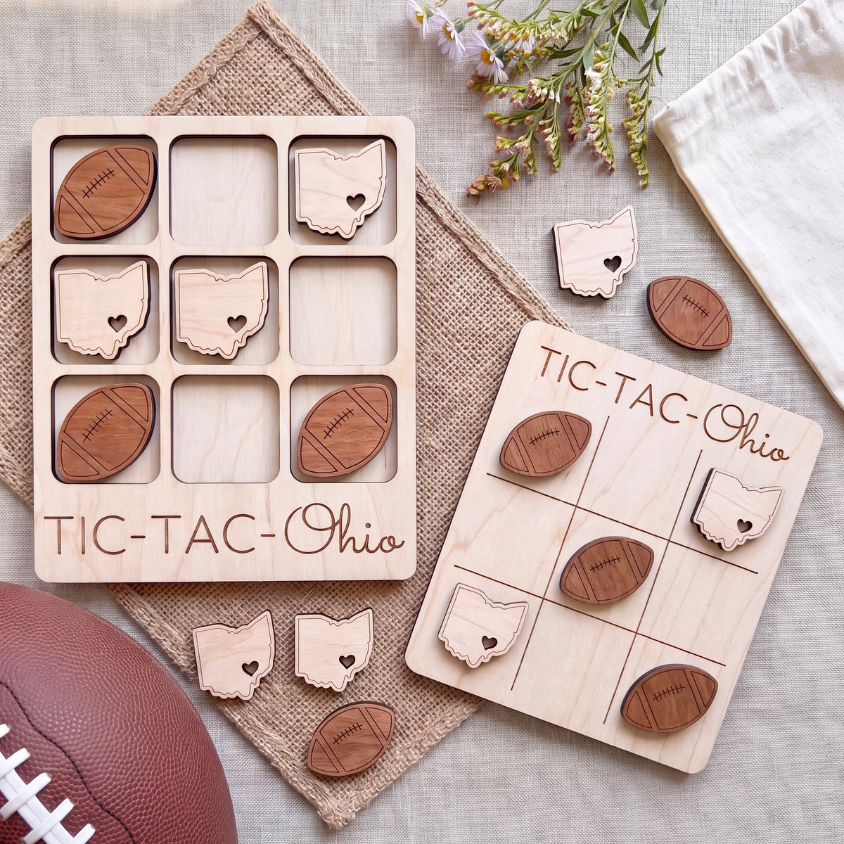 a wooden tic-tac game with Ohio state symbols, a football, and some flowers on a beige cloth.