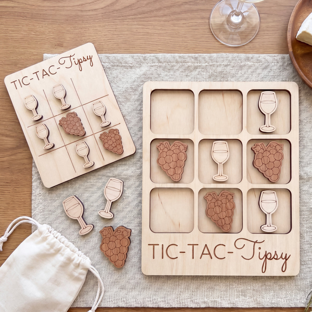 a wooden tic-tac game with wine glass and grape shapes as game pieces, placed on a wooden surface.