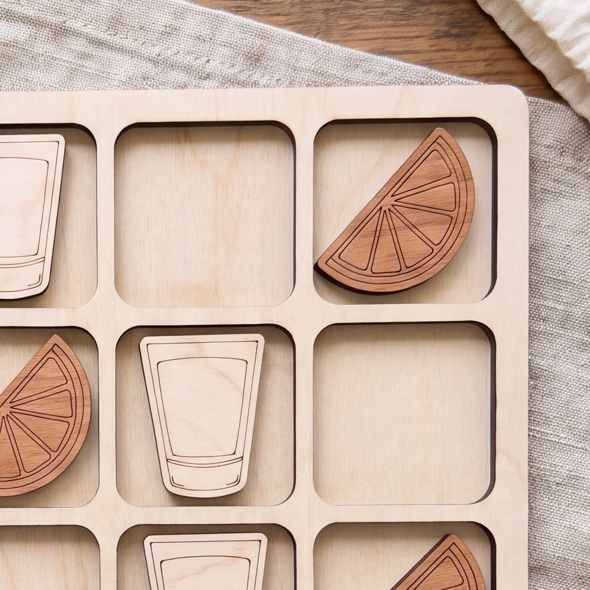 A wooden board with nine square compartments, each containing a wooden cutout of a glass and a slice of orange.
