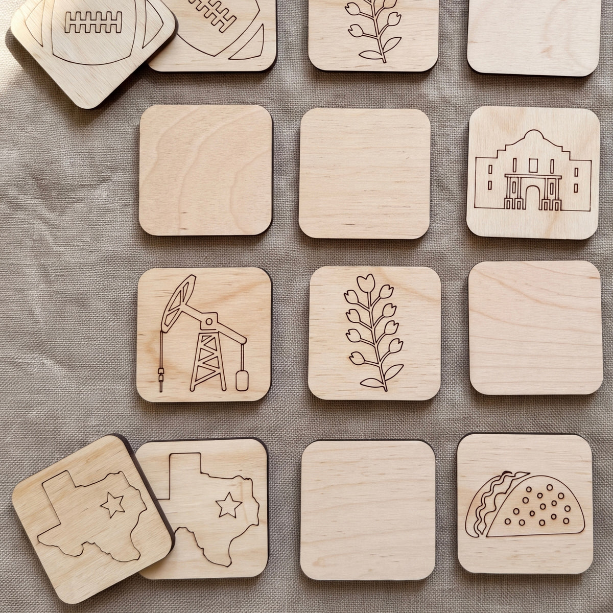 a collection of wooden coaster-shaped objects, each featuring a different design or symbol. The coasters are arranged in a grid-like pattern, with some overlapping each other. The coasters depict various themes, such as football, oil drilling, flowers, and food, showcasing a diverse range of designs and subjects.