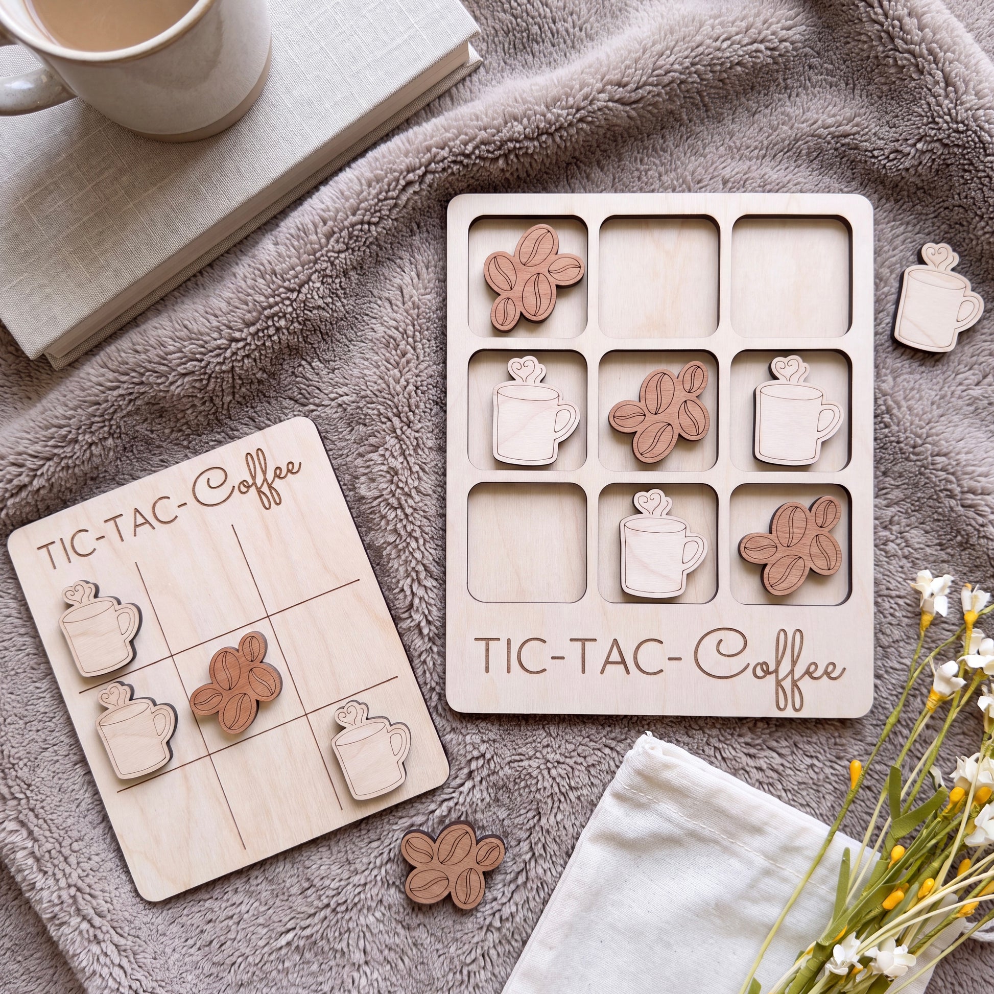 a wooden tic-tac game set with coffee cup tiles and wooden coffee cups, along with a mug and some books.