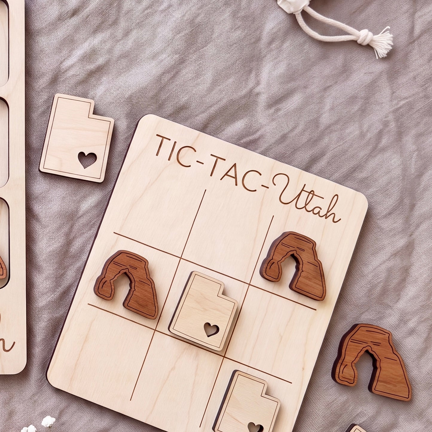 A wooden tic-tac game board with the word "TIC-TAC-UTAH" written on it, along with several wooden pieces shaped like states in Utah.