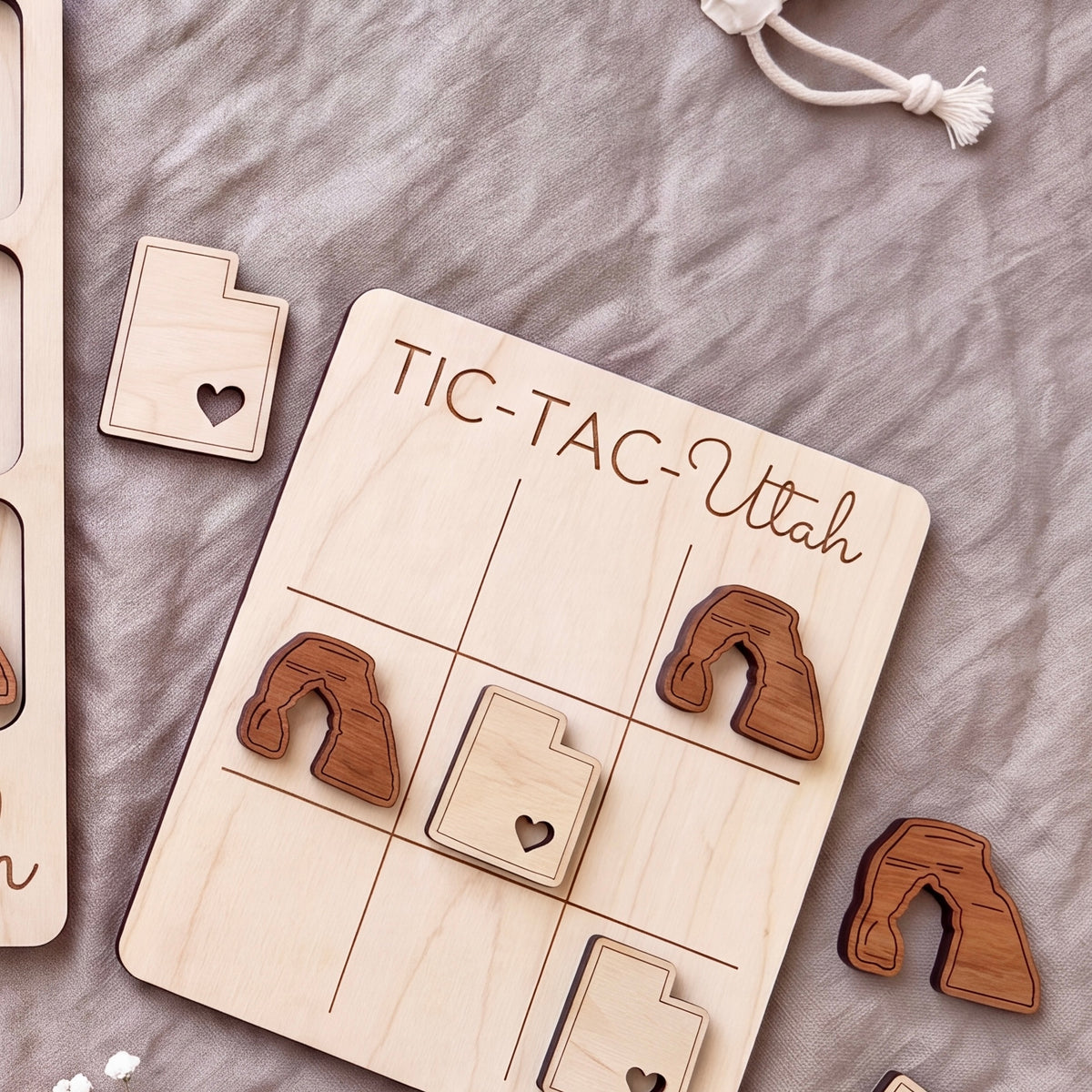 A wooden tic-tac game board with the word "TIC-TAC-UTAH" written on it, along with several wooden pieces shaped like states in Utah.