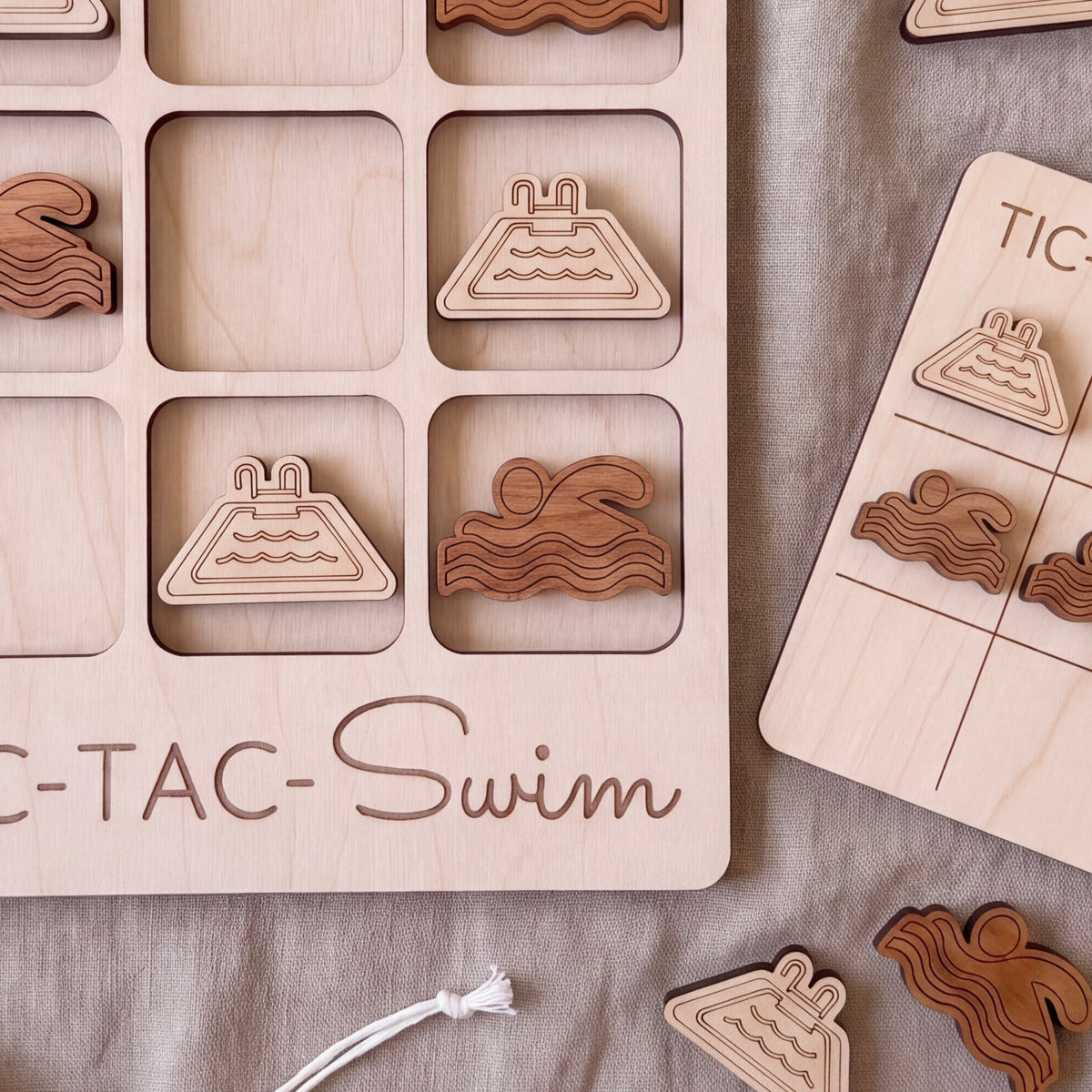 a wooden tic-tac game board with various swimming-themed tiles, including a pool and a swimmer.