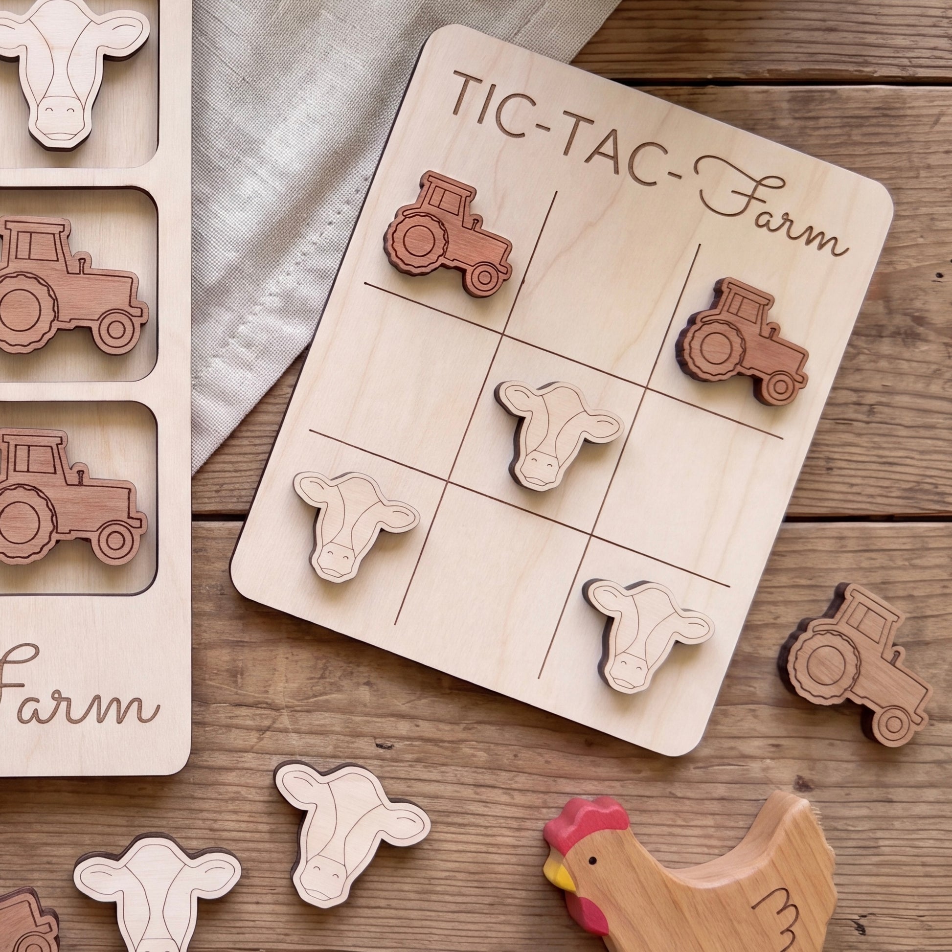 a wooden tic-tac farm game board with tractor and cow tiles, along with a wooden chicken and tractor toy set on a wooden surface.