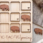 a wooden game board with a tic-tac-toe game set up, with wooden pieces shaped like buffalo or bison placed on the board.