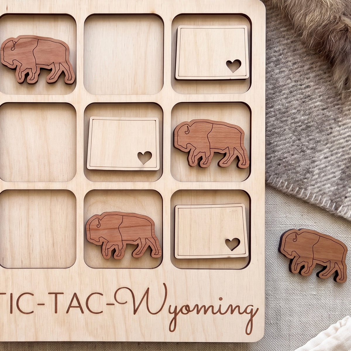 a wooden game board with a tic-tac-toe game set up, with wooden pieces shaped like buffalo or bison placed on the board.