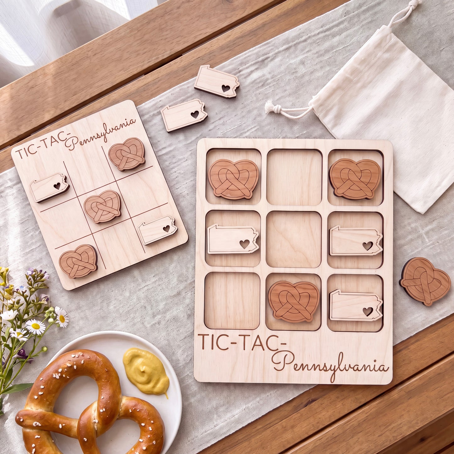 a wooden Tic-Tac game board with wooden hearts on it, along with a plate of pretzels and a white cloth.