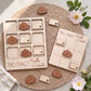 a wooden tic-tac game set with wooden pieces shaped like flowers, placed on a woven placemat. There are also some flowers and leaves in the background.