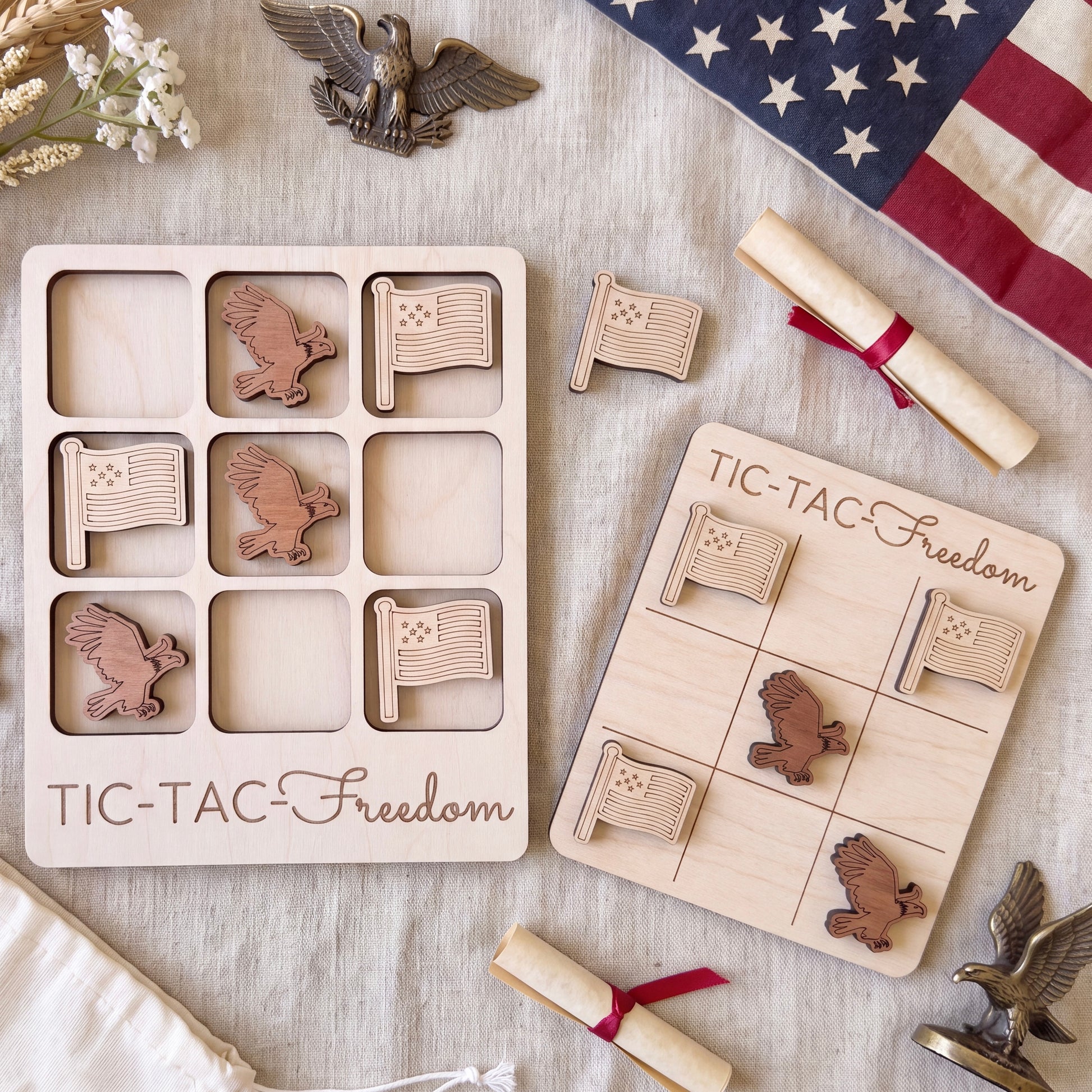 a wooden game board and a wooden game piece with eagle motifs, along with an American flag and a ribbon, all arranged on a beige cloth.