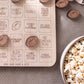 a wooden game board with various football-related terms and a bowl of popcorn on a table.