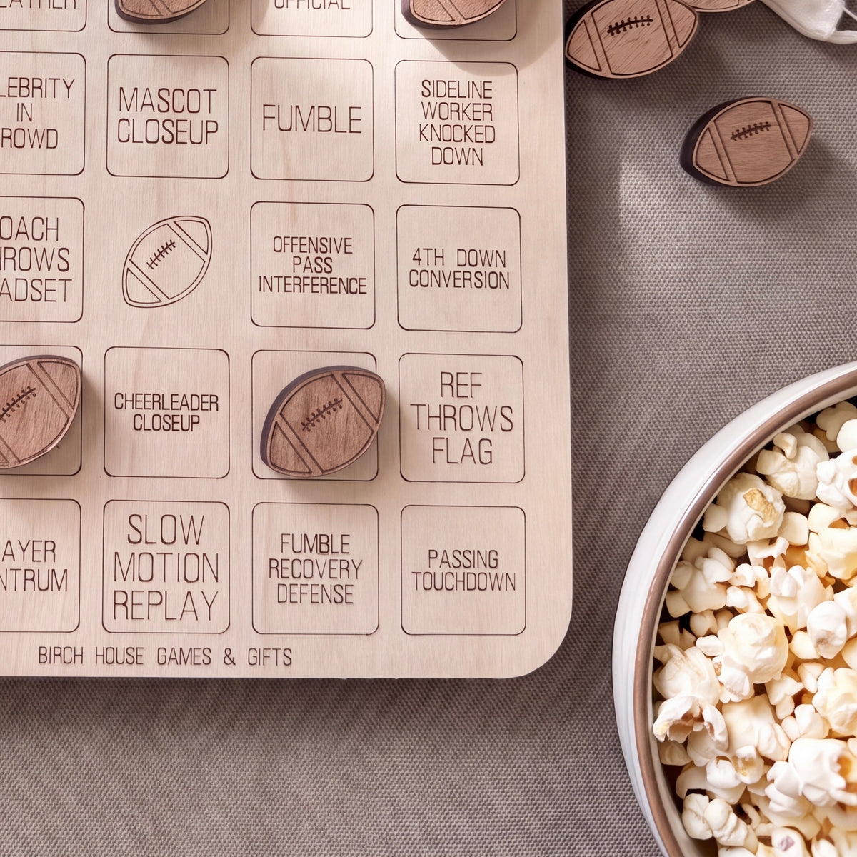 a wooden game board with various football-related terms and a bowl of popcorn on a table.