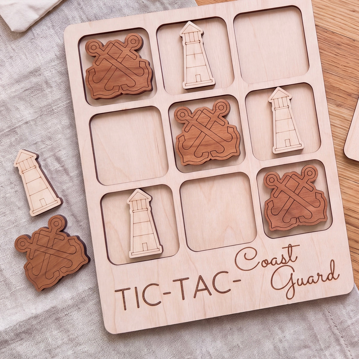 A wooden tic-tac game board with wooden pieces shaped like lighthouses and anchors, labeled "Coast Guard".