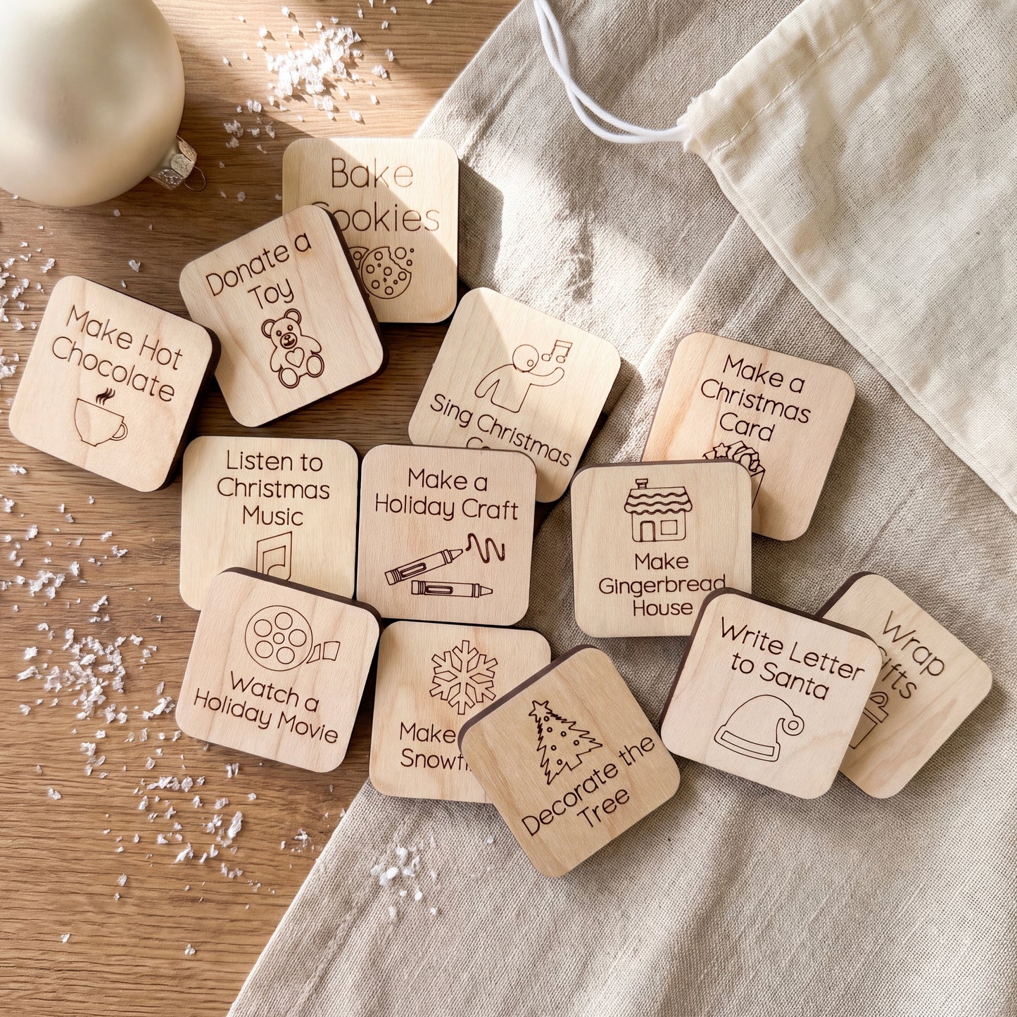 A collection of wooden stickers with various holiday-themed activities and decorations, including "Bake cookies", "Donate a toy", "Make a Christmas card", "Make a gingerbread house", "Watch a holiday movie", "Make a snowman", "Make a snowflake", "Decorate the tree", and "Write a letter to Santa".