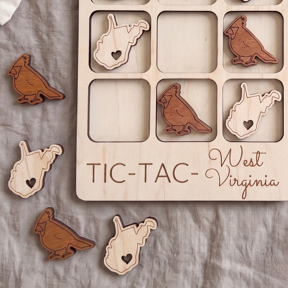 a wooden tic-tac game board with the word "West Virginia" written on it, along with several wooden bird-shaped tiles in the shape of the state of West Virginia.