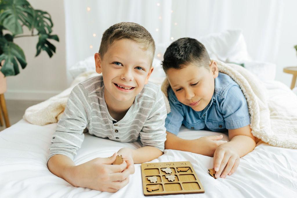 two young boys laying on a bed playing with a game