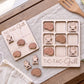 a wooden Tic-Tac-Grill game board and several wooden pieces shaped like grilled meat, arranged on a wooden surface.