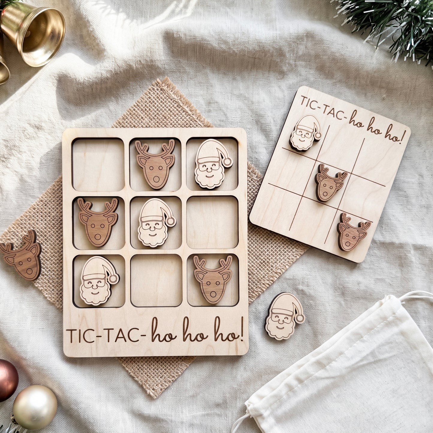 a wooden tic-tac game with Santa Claus and reindeer pieces, along with a white cloth and some Christmas ornaments.