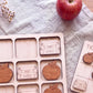 a wooden puzzle with various educational-themed pieces, including books and apples, arranged on a table. There is also a red apple and a white cloth visible in the background.