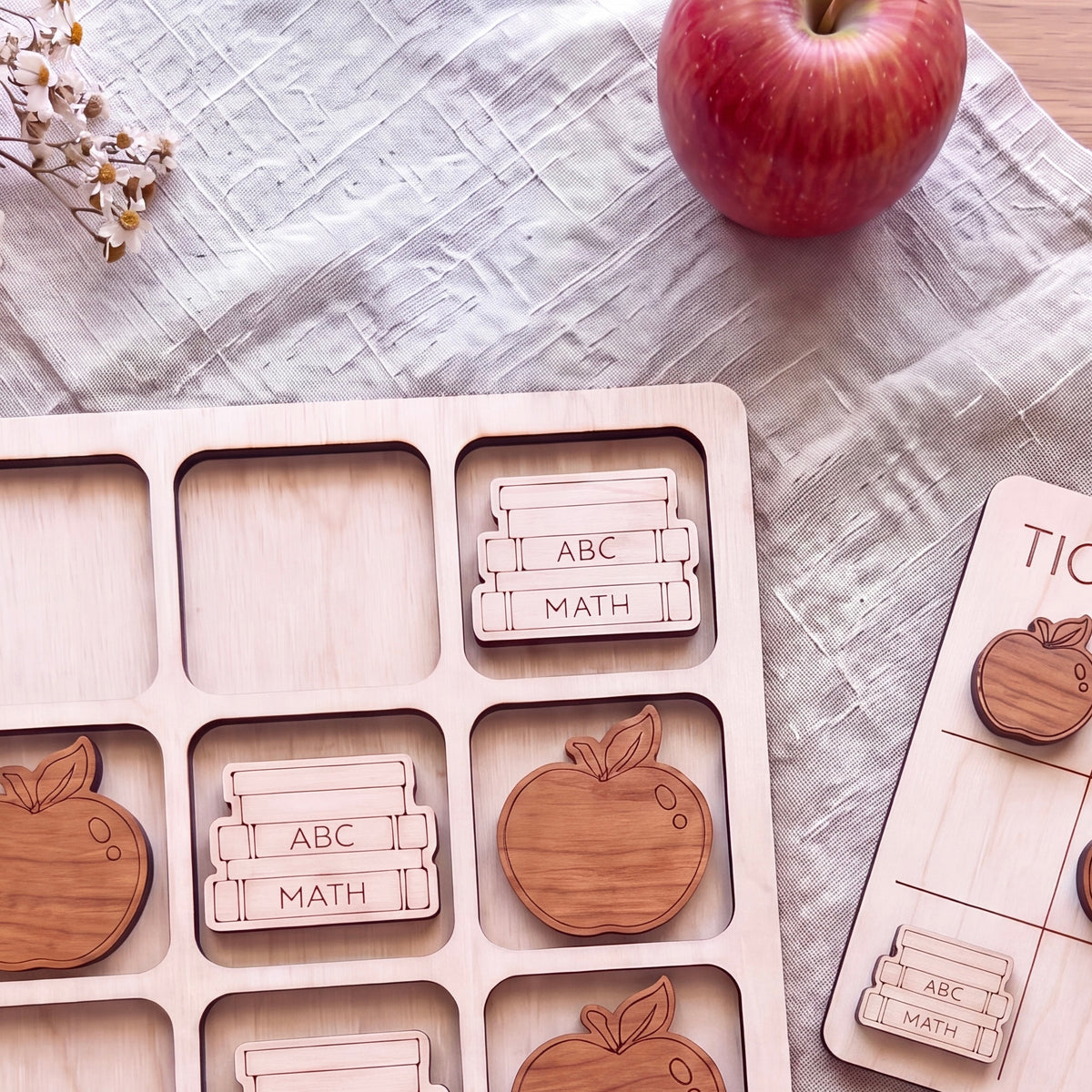 a wooden puzzle with various educational-themed pieces, including books and apples, arranged on a table. There is also a red apple and a white cloth visible in the background.