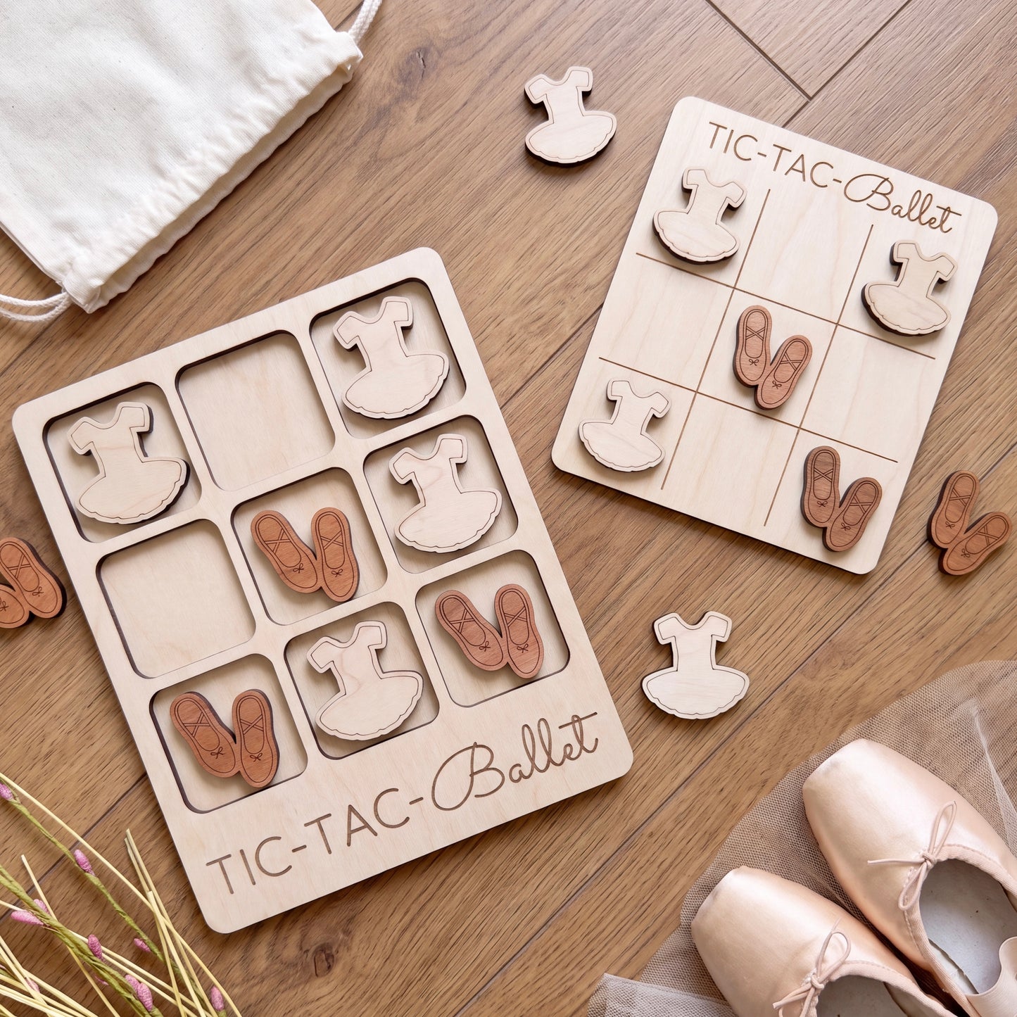 a wooden tic-tac game with ballet-themed pieces, including a game board and a game board with ballet-themed pieces. There are also some ballet shoes and a white cloth on the wooden surface.