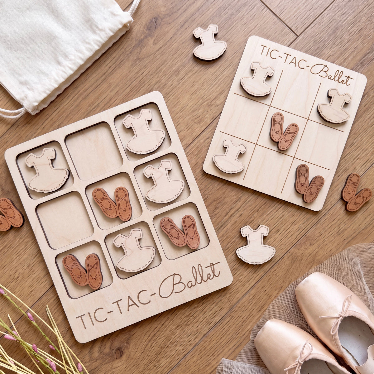 a wooden tic-tac game with ballet-themed pieces, including a game board and a game board with ballet-themed pieces. There are also some ballet shoes and a white cloth on the wooden surface.