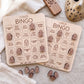 two wooden bingo cards with various scary-themed words and phrases printed on them, along with some wooden game pieces and a wooden remote control.