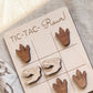 A wooden tic-tac game board with dinosaur claw and dinosaur skull tiles, along with the text "TIC-TAC-Rawr!" written on the board.