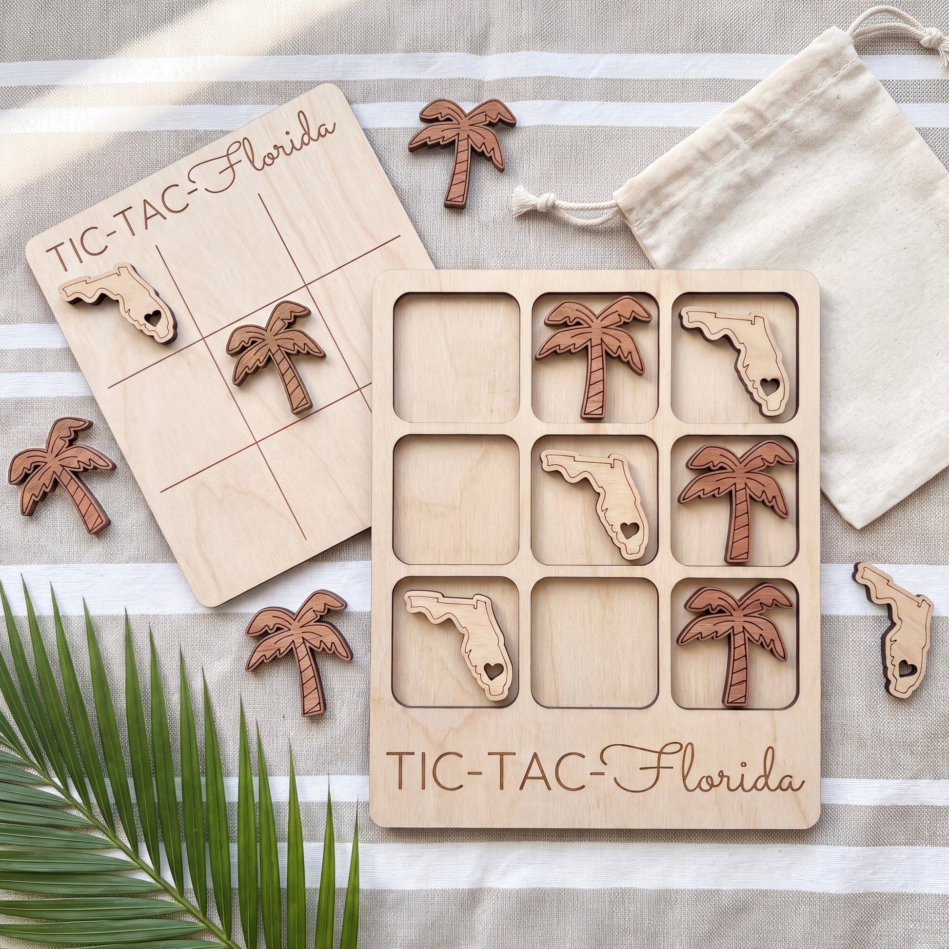 a wooden Tic-Tac-Florida game board with wooden pieces shaped like palm trees, placed on a striped towel.