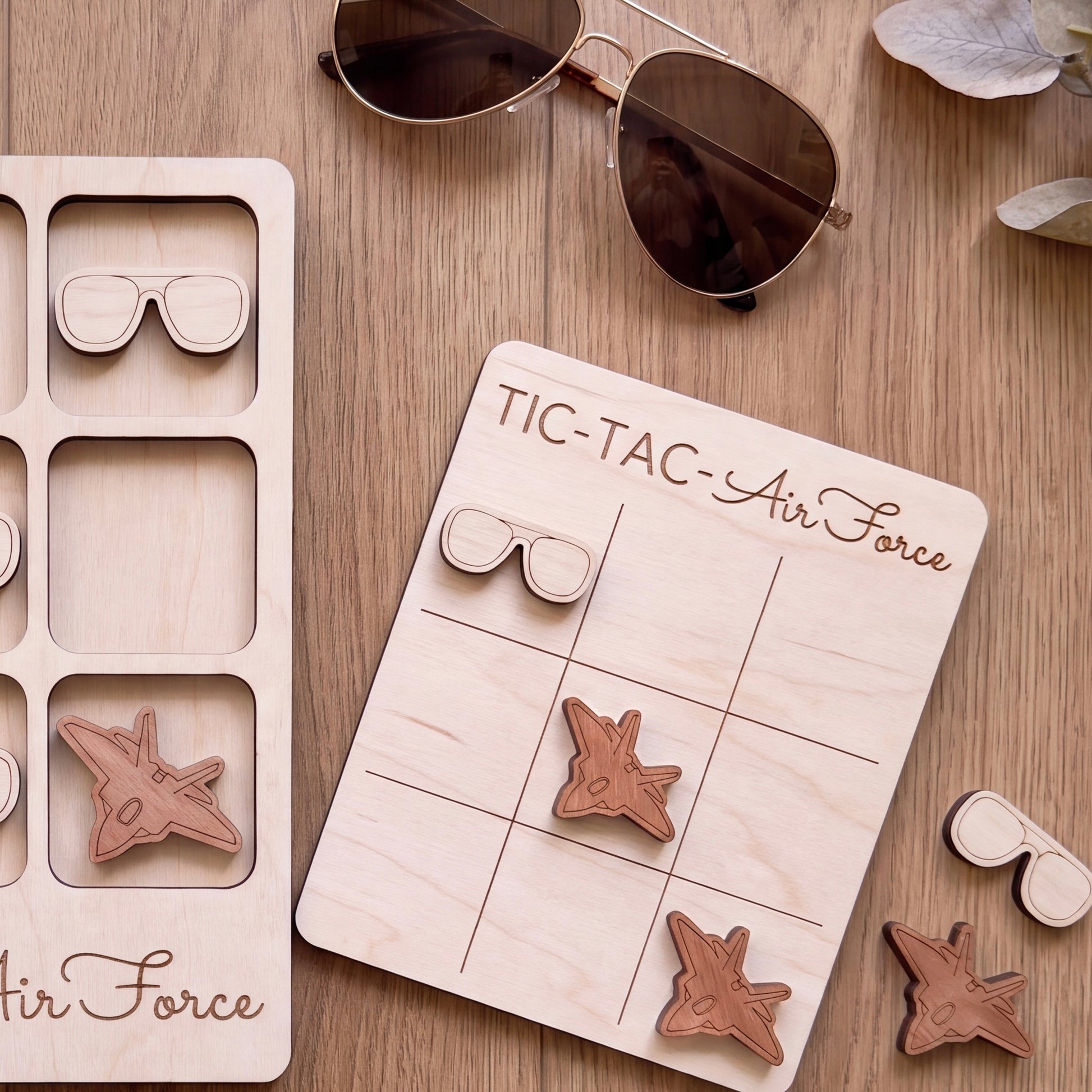a wooden tic-tac game board labeled "TIC-TAC-AIR FORCE" with wooden airplane and sunglasses pieces attached to it.